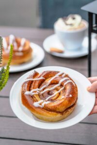 a hand holding a plate of cinnamon roll