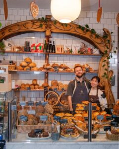 a man and woman standing in front of a display of bread