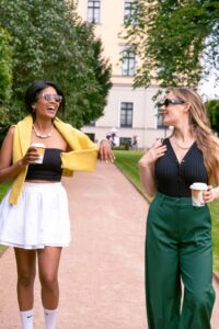 two women walking on a path with coffee cups