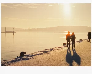 a couple of people walking on a snowy path by a body of water